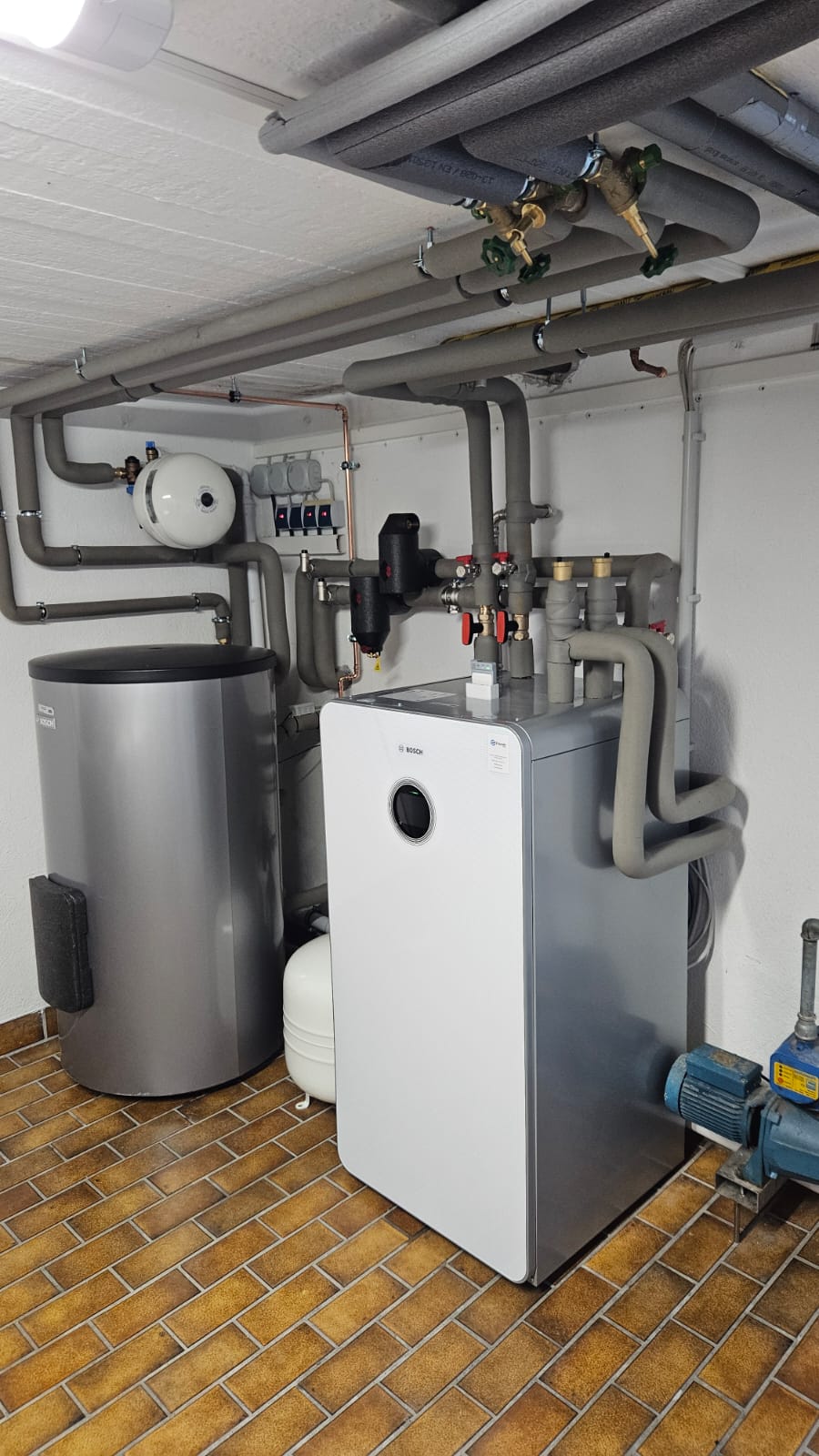 Zu sehen ist eine installierte Bosch-Wärmepumpe mit angeschlossenem Pufferspeicher und sorgfältig gedämmter Rohrleitungstechnik.